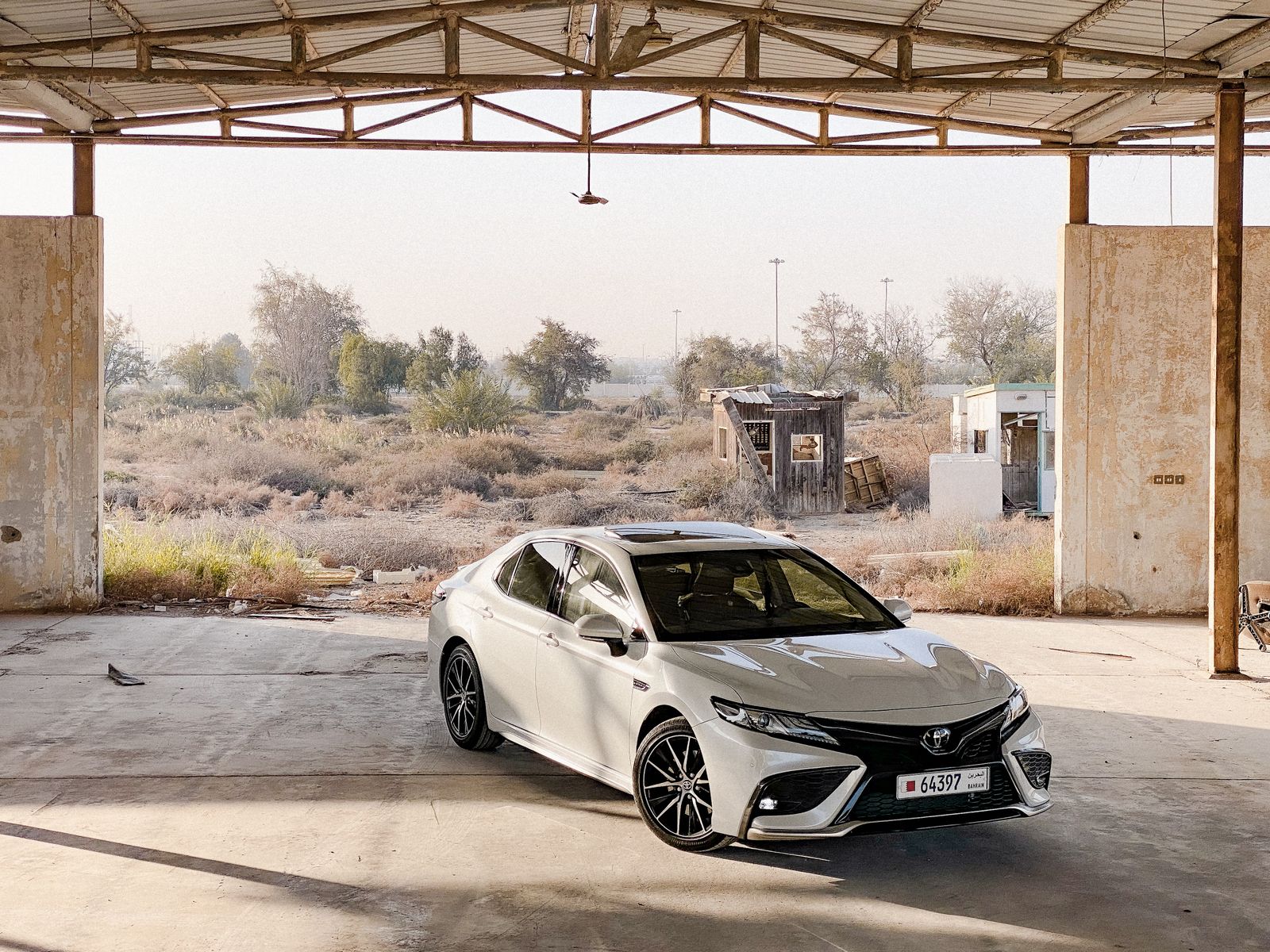 A white Toyota Camry elegantly parked in an industrial urban environment under a metal roof.