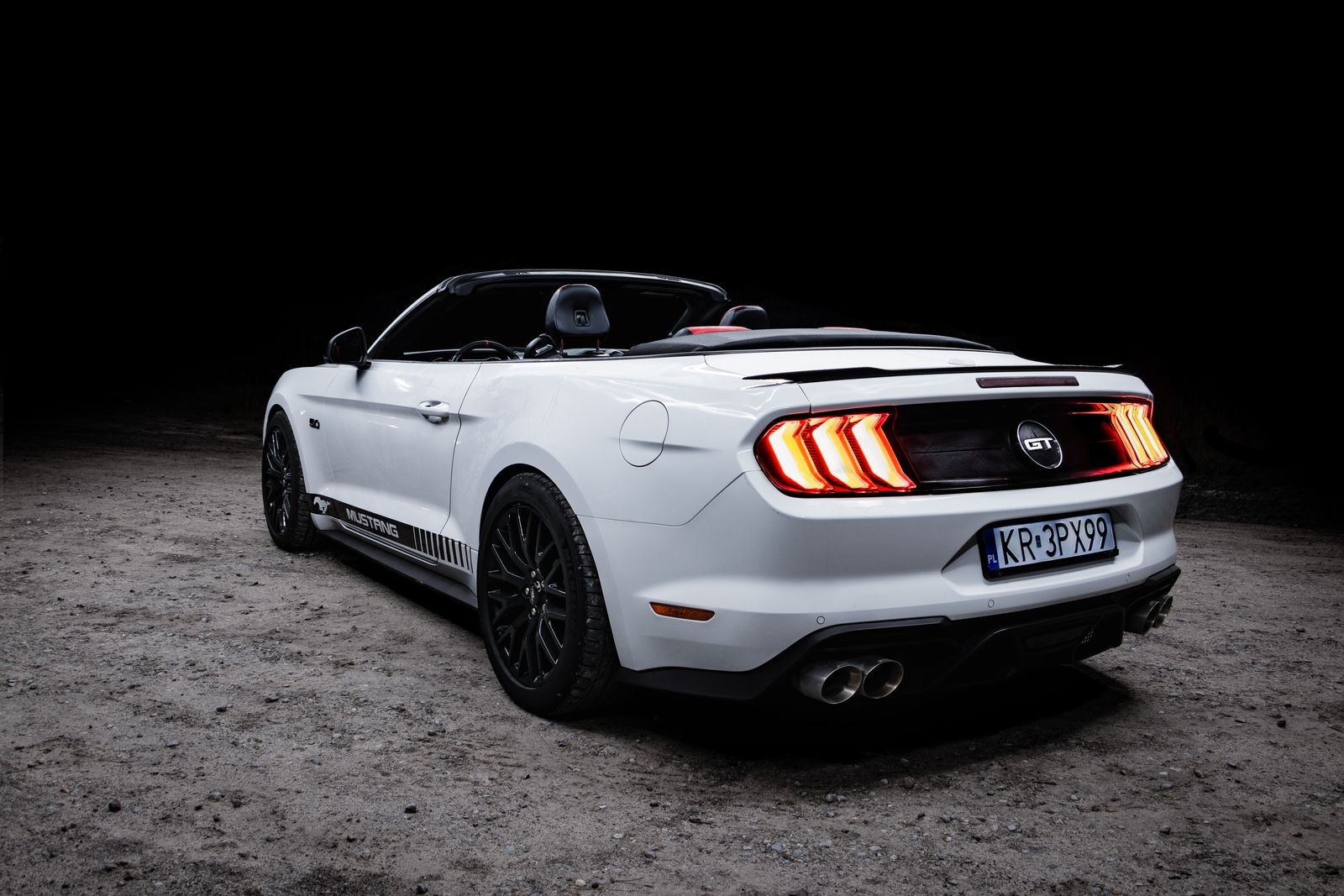 A white Ford Mustang GT convertible parked on asphalt at night with headlights on.