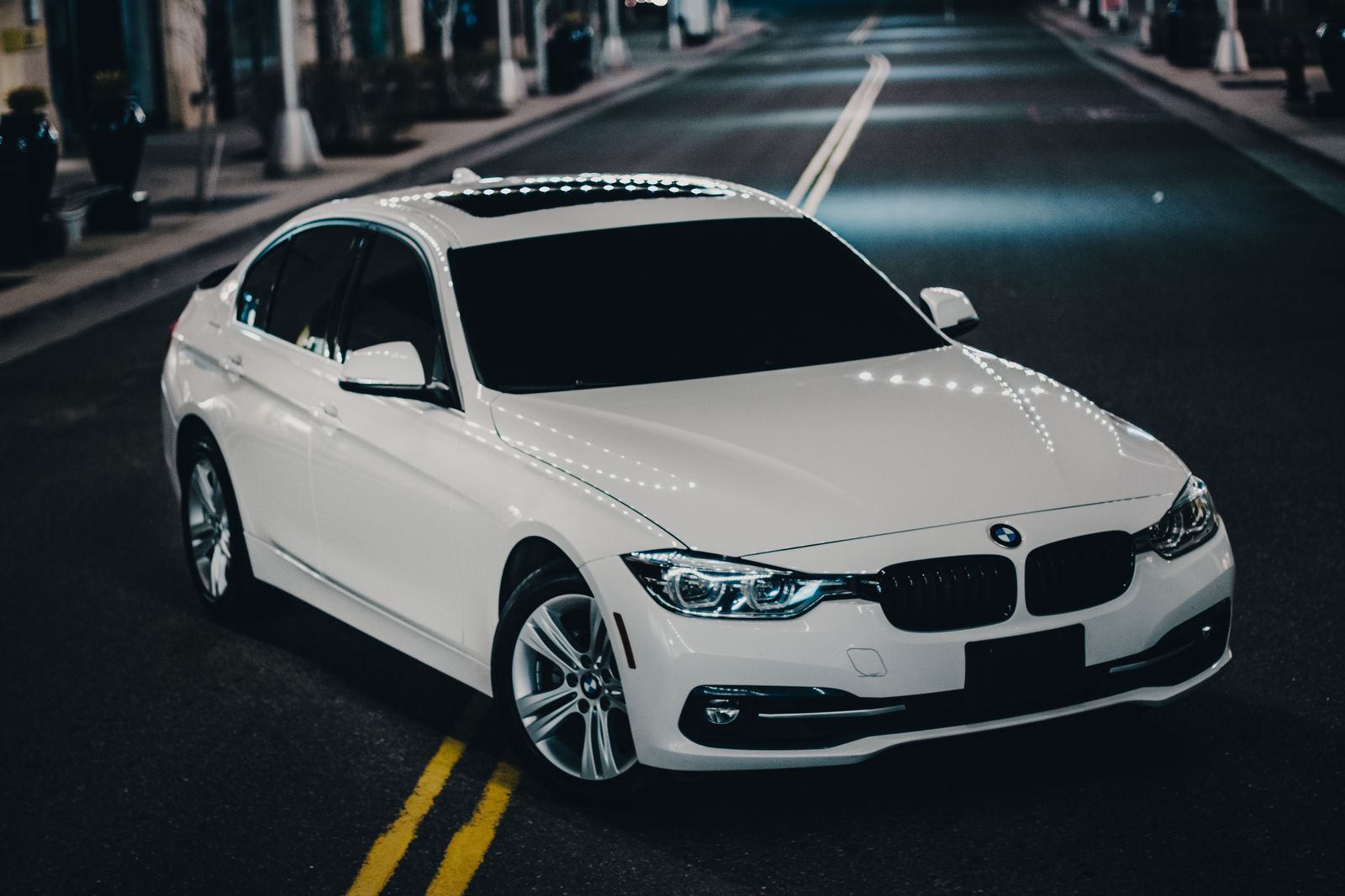 A sleek white luxury sedan parked on a city street with bright lights at night.