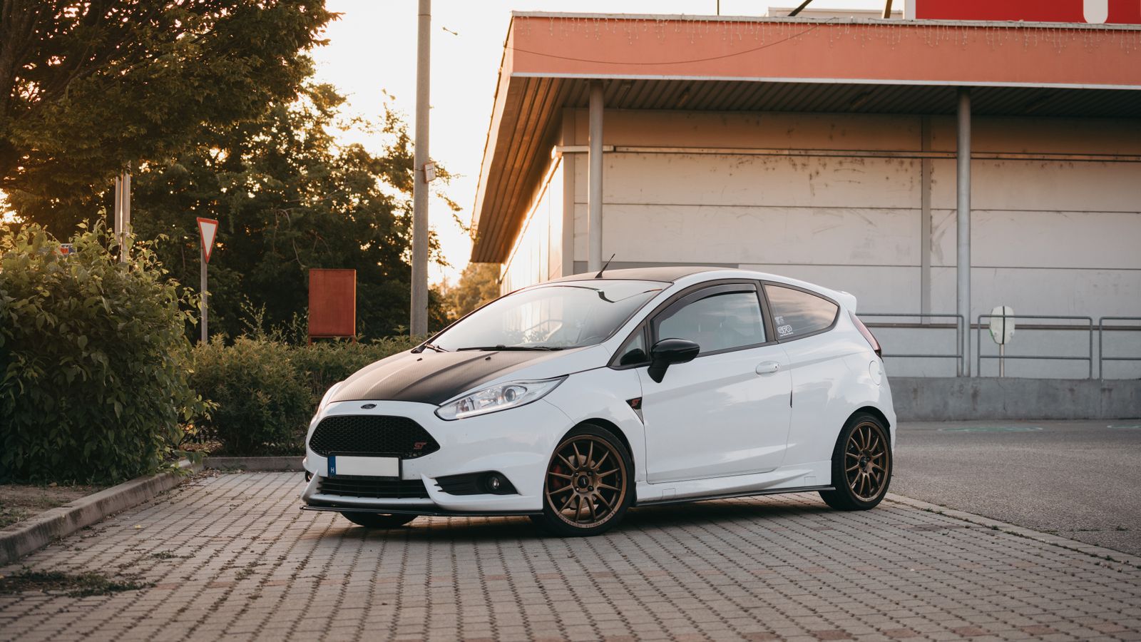 A white compact car parked outdoors near an urban building at sunset.